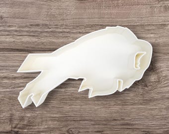 May include: White plastic cookie cutter shaped like a buffalo, a large animal with horns, standing on a wooden surface.