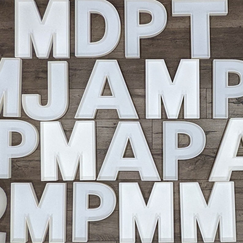 May include: White letters of the alphabet, including M, D, P, T, J, A, and others, are arranged in a random pattern on a wood background.