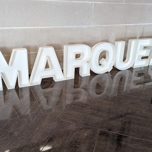 May include: White, freestanding letters spelling out the name "MARQUEZ" on a dark brown tiled floor.