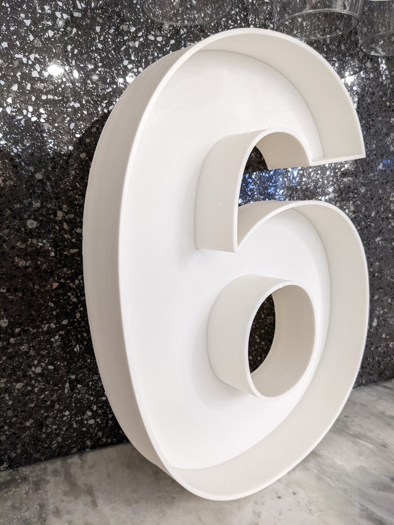 May include: A white, hollow, plastic number six. The number is large and has a three-dimensional shape.
