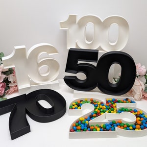 May include: White and black number shaped containers filled with colorful candies. The numbers are 16, 50, 70, 25, and 100.