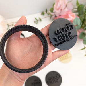 Peut inclure: Deux tampons en caoutchouc noir. L'un est un tampon rond avec le texte "The Good Stuff" et "Mary Berg" en cercle autour du texte. L'autre est un tampon rond en forme d'anneau.