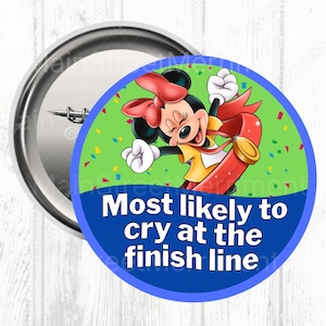 May include: A circular button badge with Minnie Mouse, wearing a yellow dress and red bow, and the text "Most likely to cry at the finish line." The background is green with confetti. The badge has a metal pin back.