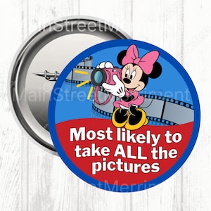 Pode incluir: Um botão redondo com Minnie Mouse em um vestido e laço rosa, segurando uma câmera rosa. O botão tem o texto "Most likely to take ALL the pictures" em um fundo vermelho, com uma borda azul e um design de tira de filme.