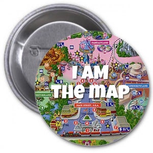 May include: A round button with a colorful map of a theme park. The map shows the different areas of the park, including Fantasyland, Tomorrowland, and Adventureland. The text "I AM THE MAP" is printed in white letters on the button.
