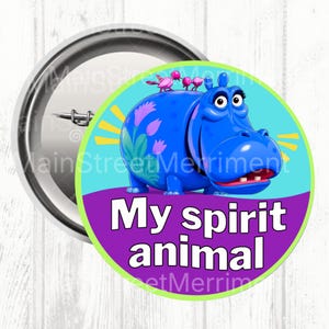 May include: A round pinback button featuring a blue cartoon hippopotamus with pink birds on its back. The hippo is set against a light blue background with yellow rays and a purple base. The text My spirit animal is printed in white letters.
