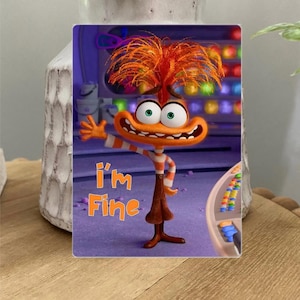 Puede incluir: Un personaje de dibujos animados con pelaje naranja y un mohawk rojo se encuentra frente a un panel de control colorido. El personaje tiene una amplia sonrisa y lleva una camisa a rayas y pantalones marrones. El texto "I'm Fine" está escrito en letras naranjas debajo del personaje.
