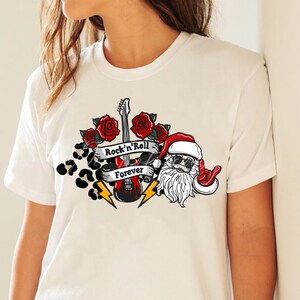 May include: White t-shirt with a graphic design featuring Santa Claus playing a guitar with the words "Rock'n'Roll Forever" on a banner.