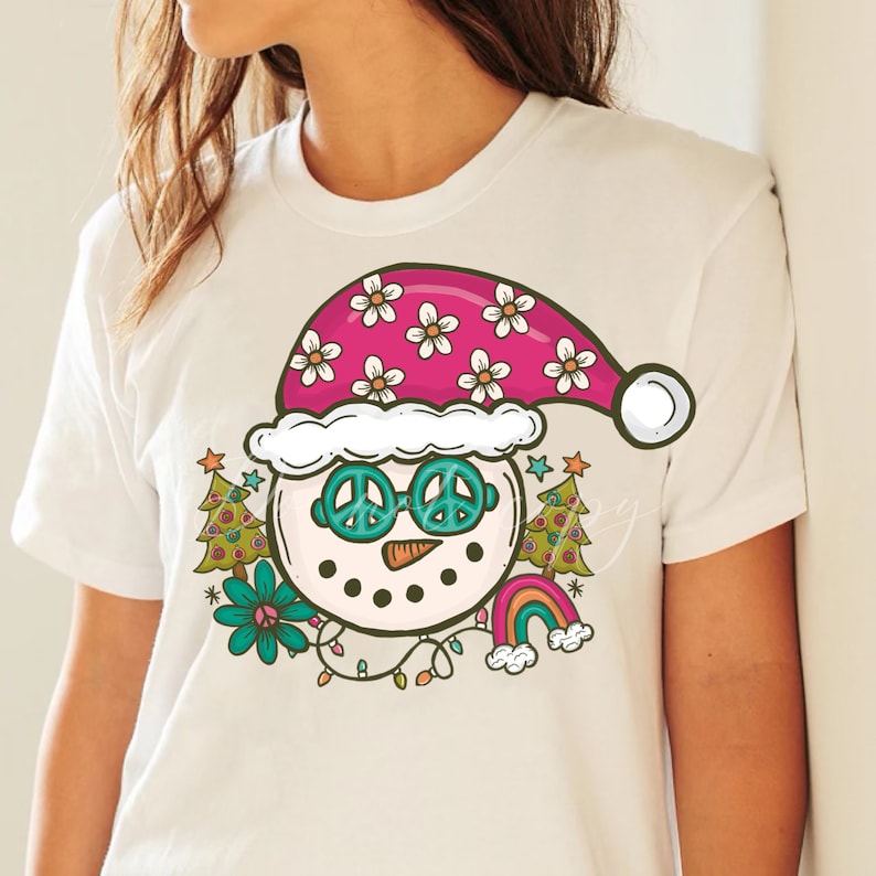 May include: White t-shirt with a colorful cartoon snowman wearing a pink and white flower hat, peace sign sunglasses, and a rainbow behind it.