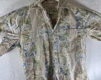 Peut inclure: Chemise à manches courtes avec un motif floral et géométrique beige, vert et bleu. La chemise a un col et une poche poitrine. Le tissu a un éclat subtil, suggérant un mélange de matières.