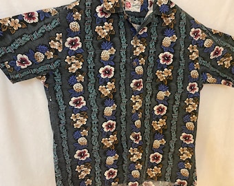 May include: A black and green short-sleeved shirt with a pineapple and floral print. The shirt has a button-up collar and a pocket on the left chest.