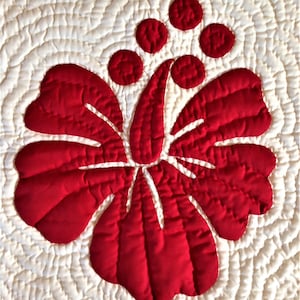 May include: A red quilted hibiscus flower with white stitching on a white quilted background.
