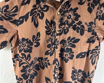 Peut inclure: Chemise boutonnée de couleur beige avec un motif floral noir. La chemise a des manches courtes, un col et une poche poitrine. Elle est suspendue à un cintre blanc.