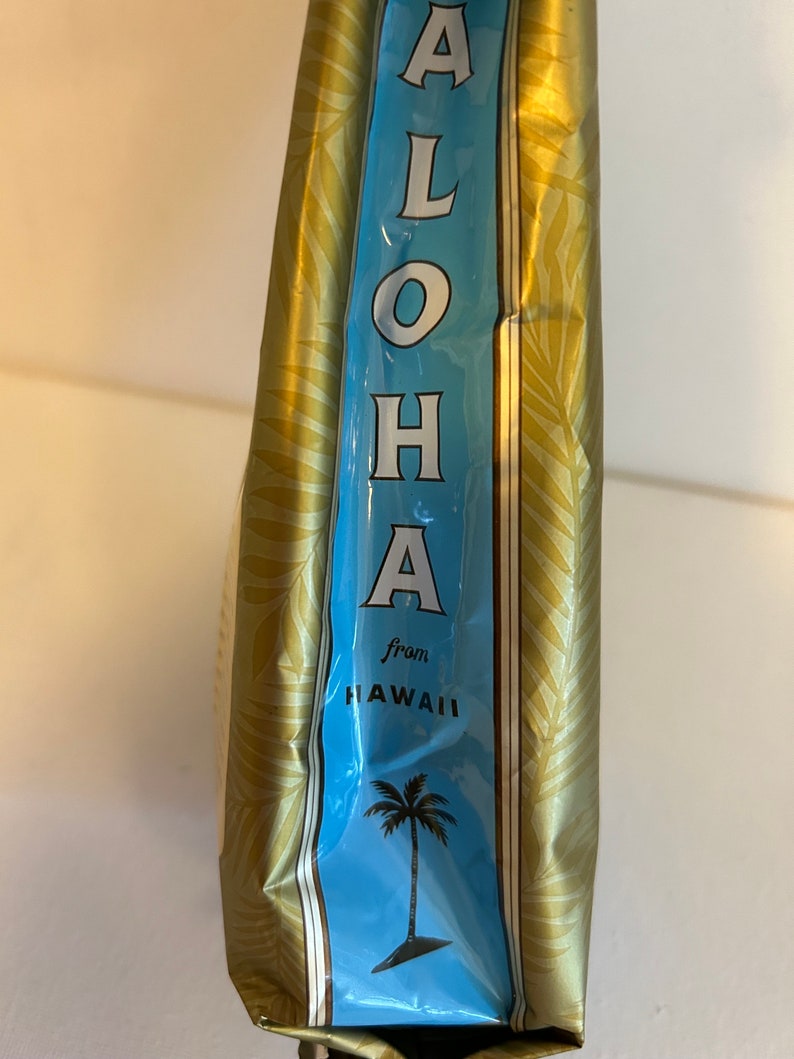 Pu&ograve; includere: Una borsa dorata con un'etichetta blu che dice "ALOHA from HAWAII" e una grafica di una palma.