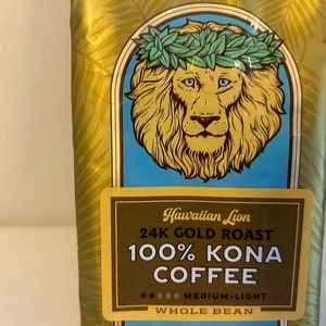 Pu&ograve; includere: Un sacchetto dorato di caff&egrave; Hawaiian Lion 24K Gold Roast 100% Kona, in grani interi, tostatura media-leggera. Il sacchetto presenta un leone con una ghirlanda di fiori verde.