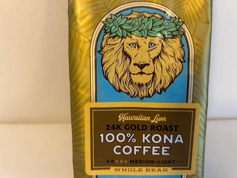 Pu&ograve; includere: Un sacchetto dorato di caff&egrave; Hawaiian Lion 24K Gold Roast 100% Kona, in grani interi, tostatura media-leggera. Il sacchetto presenta un leone con una ghirlanda di fiori verde.