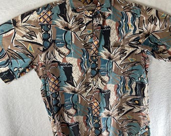 May include: Short-sleeved button-down shirt with a tropical pattern. The shirt features a repeating design of pineapples, palm trees, and geometric shapes in shades of brown, teal, and black. The brand name "Looka Street" is visible on the collar.