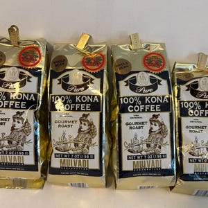 May include: Four gold bags of 100% Kona coffee, each with a gold label that reads "MV Pure 100% Kona Coffee" and "Gourmet Roast". The bags are all 7 oz (198 g) and are from the Mulvadi Corporation.