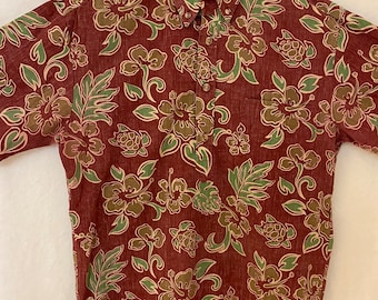 May include: A red short-sleeved button-down shirt with a green and brown floral print. The shirt has a pocket on the left side and the text "MAKAFU" and "HAWAII" on the tag.