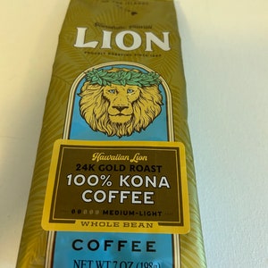 Pu&ograve; includere: Un sacchetto dorato di caff&egrave; Hawaiian Lion 24K Gold Roast 100% Kona, in grani interi, tostatura media-leggera. Il sacchetto presenta un leone con una corona di foglie e il testo "Hawaiian Lion 24K Gold Roast 100% Kona Coffee" in un riquadro giallo. Il sacchetto riporta anche il testo "Whole Bean" e "Net Wt 7 oz (198g)".