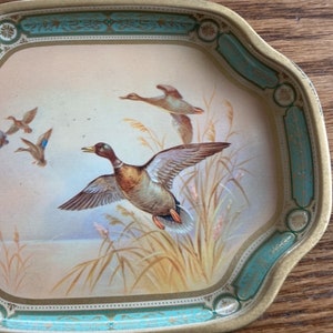 May include: A vintage metal tray with a teal and gold border. The tray features a painted scene of ducks flying over a marsh.