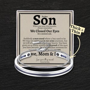 May include: A silver bracelet with a blue band and a message card that reads "To Our Son, When you wear this bracelet, always remember We Closed Our Eyes for a moment and... Suddenly a man stood where a boy used to be. We may not carry you in our arms anymore, but we will always carry you in our hearts. You have given us so many reasons to be proud of the man you have become. But the proudest moment for us was the day you became our son. Love, Mom & I Love you this much". The card also has the words "Thick & Thin" written on it.