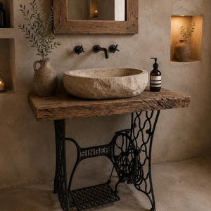 May include: A bathroom vanity featuring a rough-hewn stone vessel sink resting on a thick wooden slab countertop. The base is a black cast iron Singer sewing machine frame with a treadle. A dark soap bottle sits beside the sink.