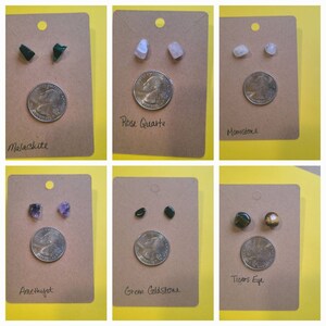 May include: Six pairs of gemstone earrings displayed on brown cards with a US quarter for scale. The stones are Malachite, Rose Quartz, Moonstone, Amethyst, Green Goldstone, and Tiger's Eye.