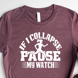 May include: Heather maroon t-shirt with the text "IF I COLLAPSE PAUSE MY WATCH" in white. A white graphic of a running person is in the center of the text. The shirt is knotted at the bottom.