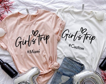 May include: Two pink and white t-shirts with the text "Girl's Trip" and a heart symbol. The pink shirt has the text "#Miami" and the white shirt has the text "#Custom".