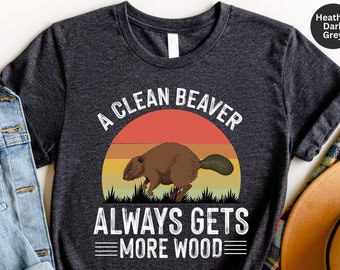 May include: A dark heather grey t-shirt with a vintage-style graphic of a beaver with the text "A Clean Beaver Always Gets More Wood".