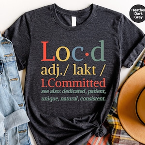 May include: Heather dark grey t-shirt with the word "Loc-d" defined as "committed" in a colorful, retro font.