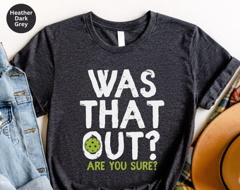 May include: Heather dark grey t-shirt with white text that reads "Was that out? Are you sure?" and a green pickleball graphic.