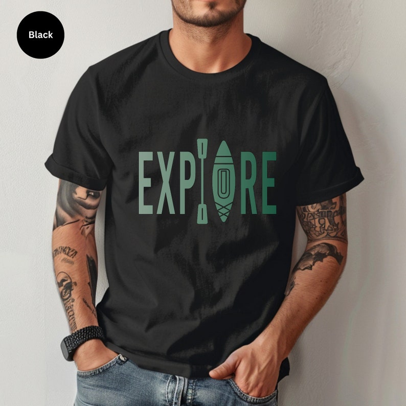 Puede incluir: Camiseta negra con la palabra "EXPLORE" en un degradado de color verde, con un gr&aacute;fico de kayak y remo. La camiseta est&aacute; hecha de un material suave y es adecuada para actividades al aire libre. La camiseta es negra.