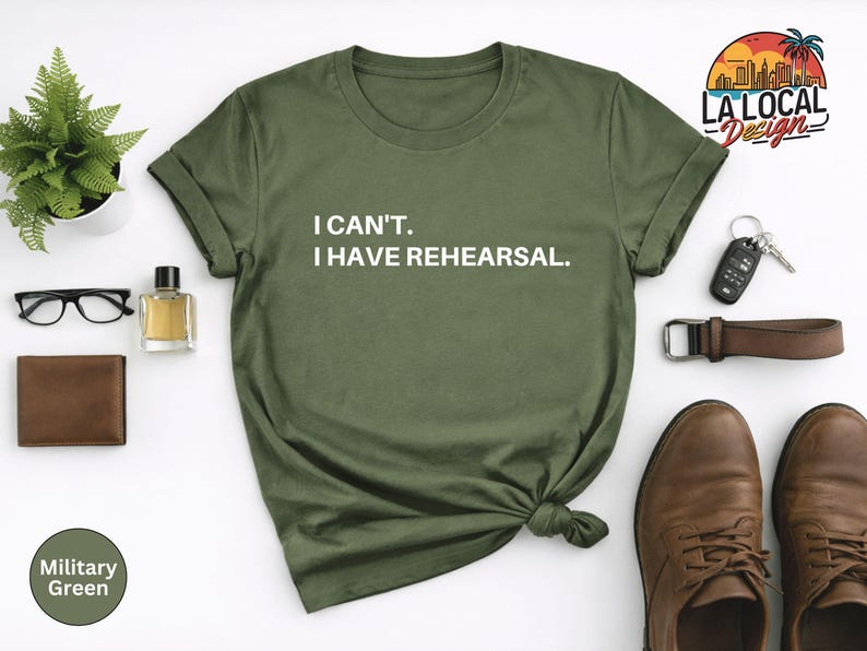 May include: Olive green t-shirt with the text "I CAN'T. I HAVE REHEARSAL." in white. The shirt is styled with a brown belt, shoes, wallet, glasses, and a small potted plant. The shirt is a military green color.