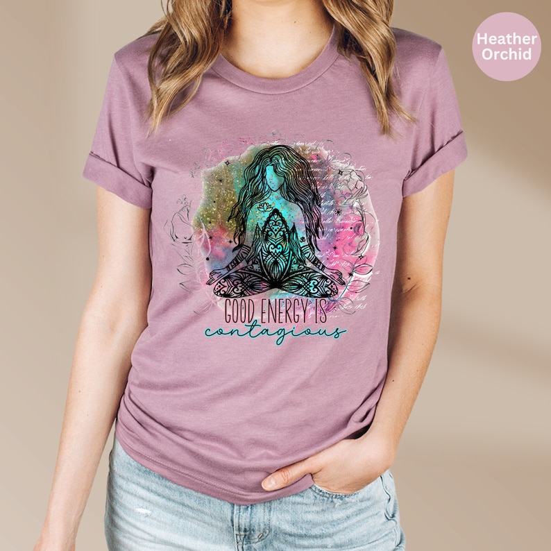 Peut inclure: T-shirt couleur orchid&eacute;e avec une illustration d'une personne assise en position de yoga. Le design comprend un fond aquarelle color&eacute; et le texte "GOOD ENERGY IS contagious" en turquoise. Manches retrouss&eacute;es.