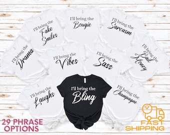 May include: Nine white t-shirts with black text that reads "I'll bring the" followed by a different phrase on each shirt. The phrases are: "Drama", "Fake Smiles", "Bougie", "Sarcasm", "Vibes", "Sass", "Laughs", "Bling", and "Champagne". One black t-shirt with white text that reads "I'll bring the Bling". The shirts are arranged in a circle on a white wooden background. The text "29 PHRASE OPTIONS" is at the bottom of the image.