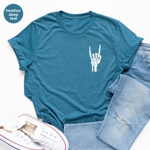 May include: A heather deep teal t-shirt with a white skeleton hand graphic making a rock and roll gesture. The shirt is folded, with blue jeans and white sneakers in the background.