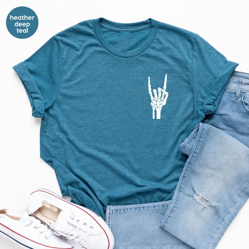 May include: A heather deep teal t-shirt with a white skeleton hand graphic making a rock and roll gesture. The shirt is folded, with blue jeans and white sneakers in the background.