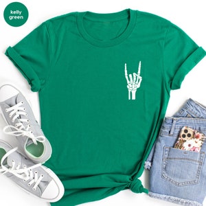 May include: Kelly green t-shirt with a white skeleton hand graphic making a rock and roll gesture. The shirt is paired with gray sneakers and denim shorts. The shirt's color is labeled "kelly green" in a circle.