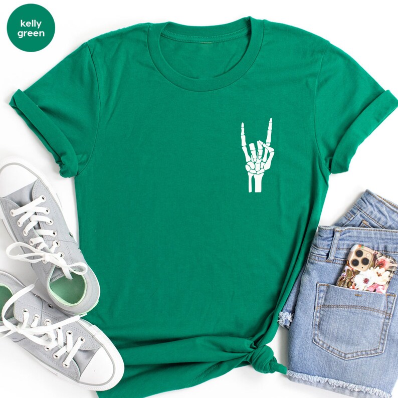 May include: Kelly green t-shirt with a white skeleton hand graphic making a rock and roll gesture. The shirt is paired with gray sneakers and denim shorts. The shirt's color is labeled "kelly green" in a circle.