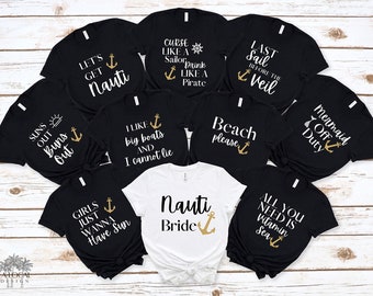 May include: A set of nine black t-shirts with gold text and anchor designs. The shirts feature nautical-themed phrases like "Let's Get Nauti", "Suns Out Buns Out", "Curse Like a Sailor Drink Like a Pirate", "Last Sail Before the Veil", "I Like Big Boats and I Cannot Lie", "Beach Please", "Mermaid Off Duty", "Girls Just Wanna Have Sun", and "All You Need is Vitamin Sea". One white t-shirt with gold text and an anchor design reads "Nauti Bride".