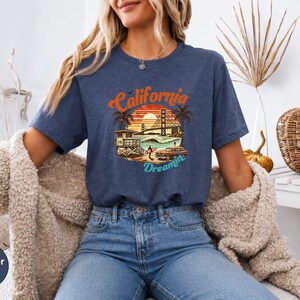 May include: Heather navy blue t-shirt with a California Dreamin' graphic. The design features a sunset, palm trees, the Golden Gate Bridge, and a vintage car. The shirt is a relaxed fit and made of soft material.