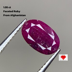 Pode incluir: Uma gema de rubi facetada do Afeganistão, segurada por pinças. A gema em forma oval é de cor vermelha profunda com facetas brancas. O texto na imagem diz "1,05 ct Faceted Ruby From Afghanistan."