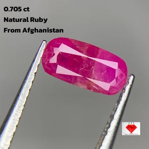 Può includere: Una vibrante gemma di rubino naturale, sfaccettata, di forma ovale, del peso di 0,705 ct, tenuta da una pinzetta. Il testo sull'immagine recita "Natural Ruby From Afghanistan."