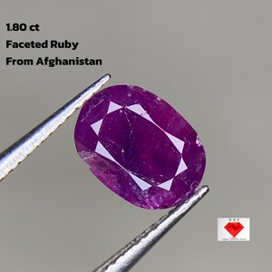 Puede incluir: Un rubí facetado de forma ovalada, sujeto con pinzas. La gema de color magenta oscuro es de Afganistán y pesa 1,80 ct. El texto en la imagen dice "Faceted Ruby From Afghanistan".