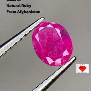 Puede incluir: Un rubí natural ovalado de Afganistán, sujeto con pinzas. La piedra preciosa es de color rojo rosado intenso y pesa 0,335 ct. El texto de la imagen dice "0.335 ct Natural Ruby From Afghanistan".