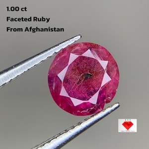 Pode incluir: Uma gema de rubi facetada, segurada por pinças, com o texto "1.00 ct Faceted Ruby From Afghanistan". O rubi é de cor vermelha profunda com um padrão em forma de estrela no centro.