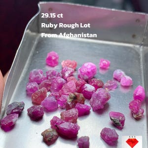 Puede incluir: Un lote de piedras preciosas de rubí en bruto, con un peso de 29,15 ct, presentado en una bandeja metálica. Los rubíes son de varios tonos de rosa y rojo. El texto de la imagen dice "Ruby Rough Lot From Afghanistan."