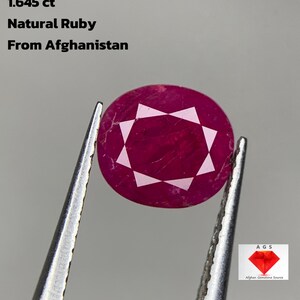 May include: A natural ruby gemstone from Afghanistan, held by tweezers. The round, faceted ruby is a deep red colour with white facets. Text on the image reads: "1.645 ct Natural Ruby From Afghanistan."